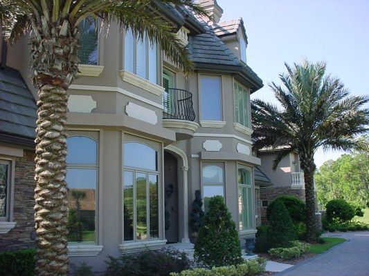 Elegant two-story house with bay windows, palm trees, and a tiled roof, under a blue sky.
