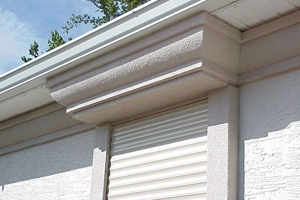 Exterior building detail with decorative molding above a shutter. Beige and white.