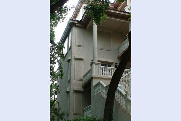 Beige stucco multi-story building with columns and a balcony, trees partially obscure the view.