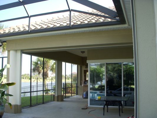 Patio with screen enclosure, tile roof, sliding glass door, and view of a lake.
