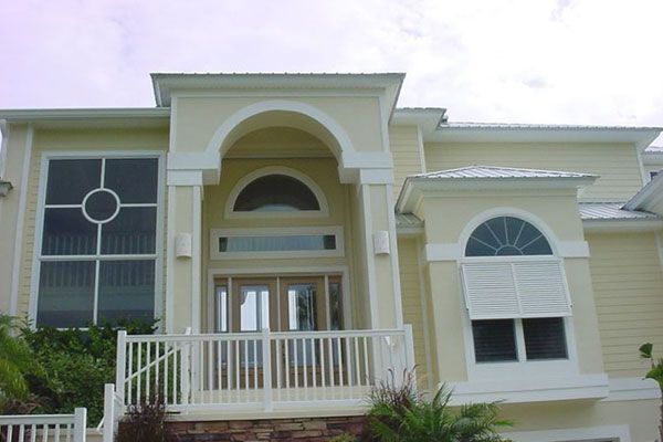 Yellow house with white trim, arched entryway and window details, and a small porch.