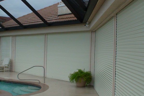 Exterior view of a pool area with closed, light-colored rolling shutters.
