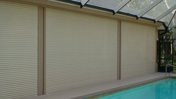 Beige rolling shutters covering a pool enclosure wall.