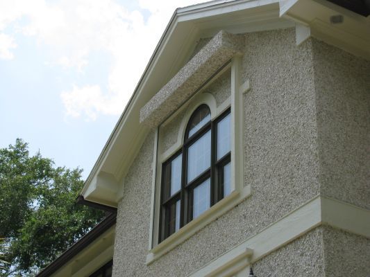 Two-story house with stucco exterior. Arched window has beige trim and a fabric awning.