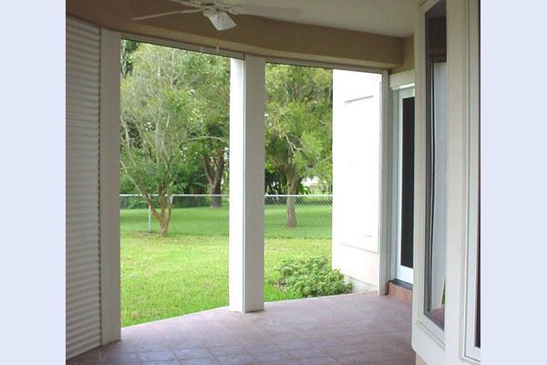 Covered patio with columns, overlooking a grassy yard and trees. White shutters on the left.