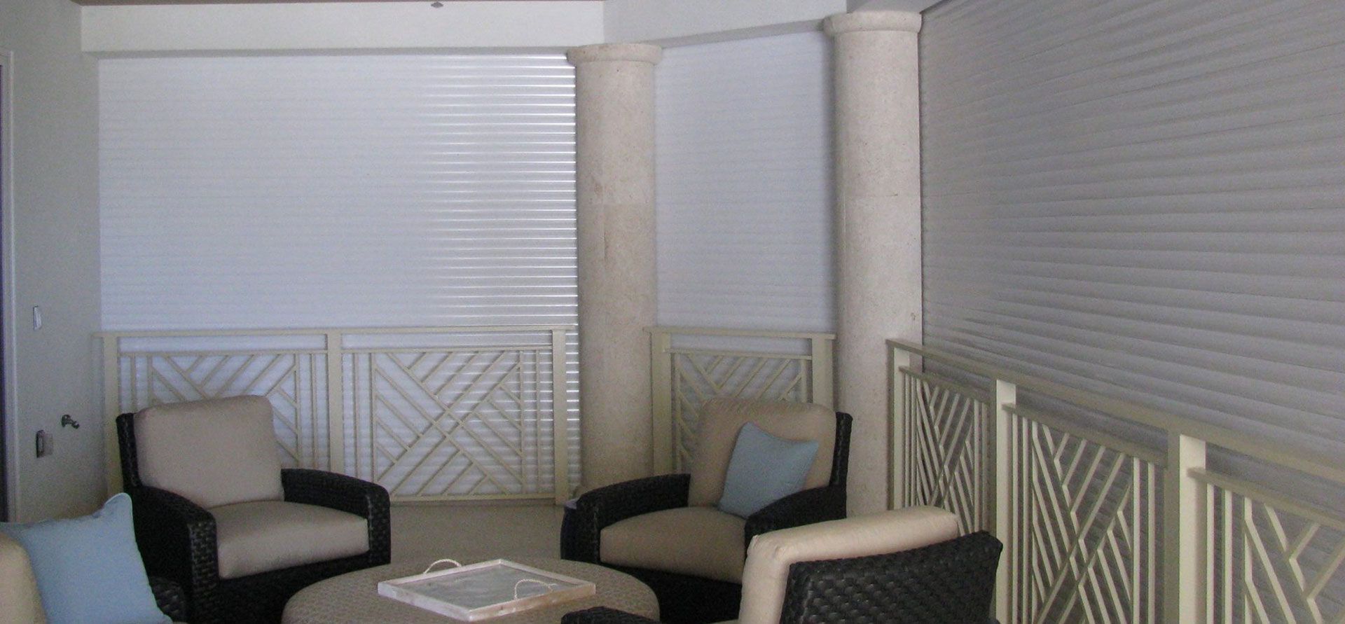 A seating area with four armchairs, a central table, and two stone pillars in front of white paneled walls and railings.