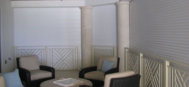 A seating area with four armchairs, a central table, and two stone pillars in front of white paneled walls and railings.