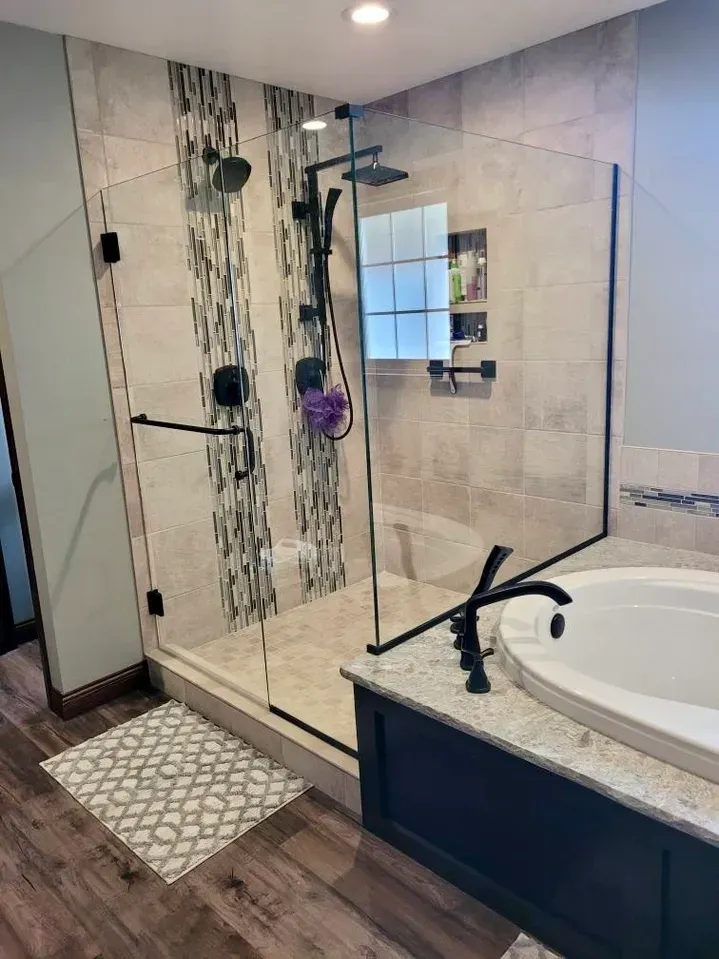 A walk-in shower with beige tile, a decorative vertical accent strip, and black fixtures, next to a soaking tub.