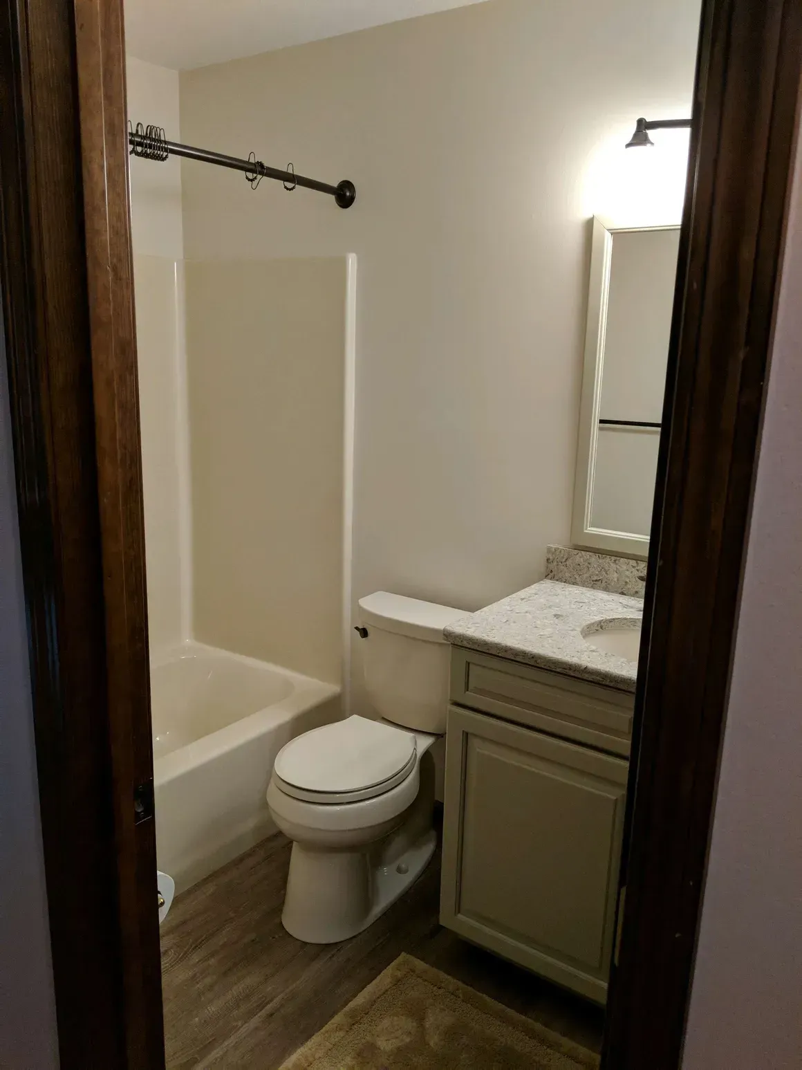 A neutral-toned bathroom with a shower-tub combo, a toilet, a vanity with a white countertop, and a wall mirror.