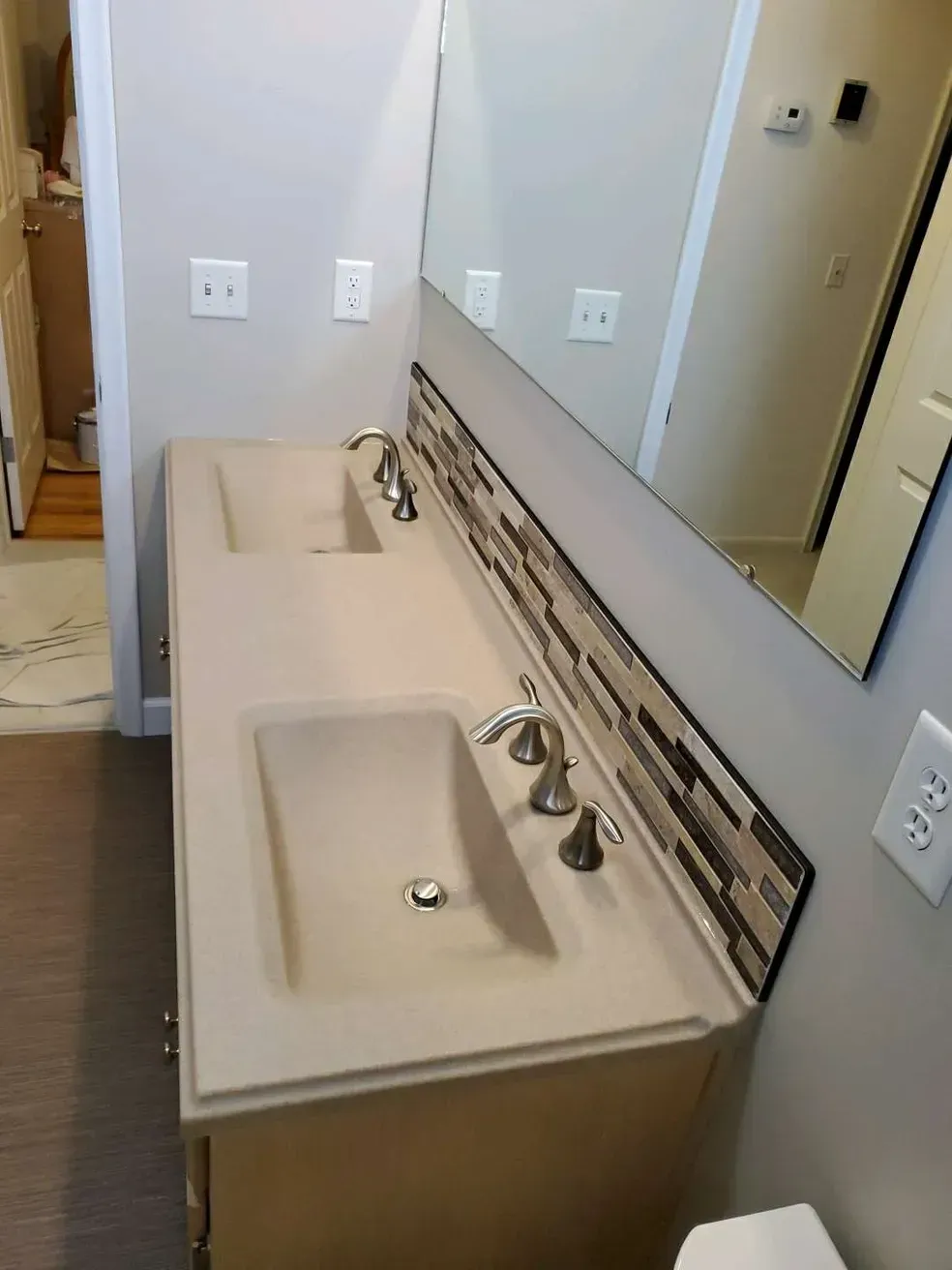 A double-sink bathroom vanity with light beige integrated sinks, a tiled backsplash, and a wall-mounted mirror.