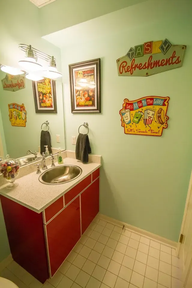A bathroom with mint green walls, a red vanity cabinet, a silver sink, and retro-style diner wall art.