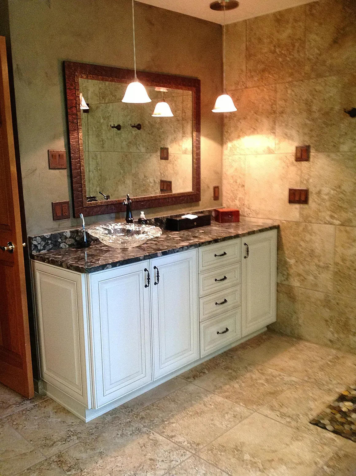 A bathroom vanity with a white cabinet, stone countertop, sink, and mirror against a tiled wall.
