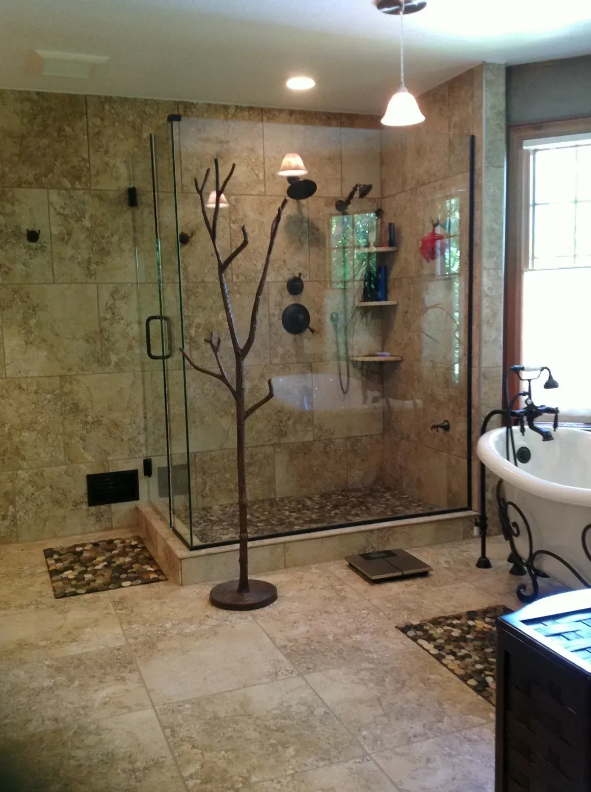 A bathroom featuring a large glass-enclosed shower with stone tile, a decorative metal branch towel rack, and a bathtub.