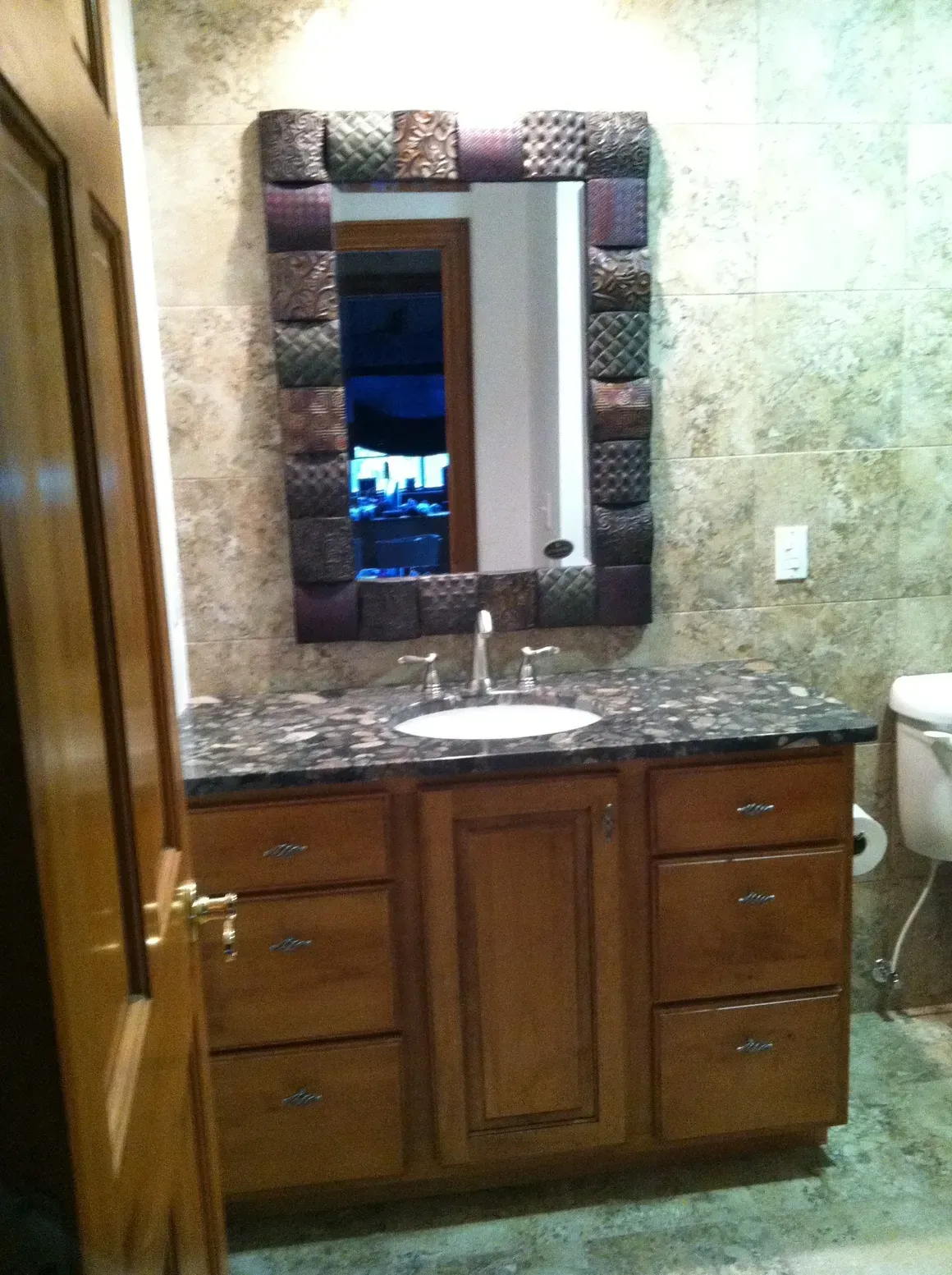 Bathroom vanity with dark wooden cabinets, granite countertop, and a decorative mirror on a tiled wall.