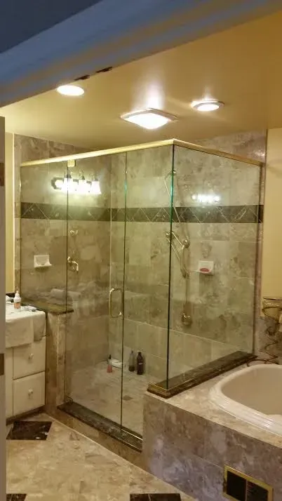 A marble-tiled bathroom featuring a glass shower enclosure and a built-in soaking tub under recessed lighting.