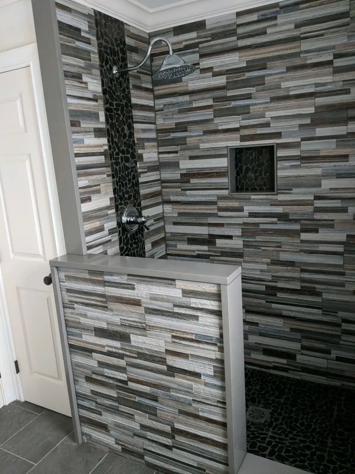 A walk-in shower with a low stone-tiled half wall, dark stacked stone walls, a rainfall showerhead, and a niche.