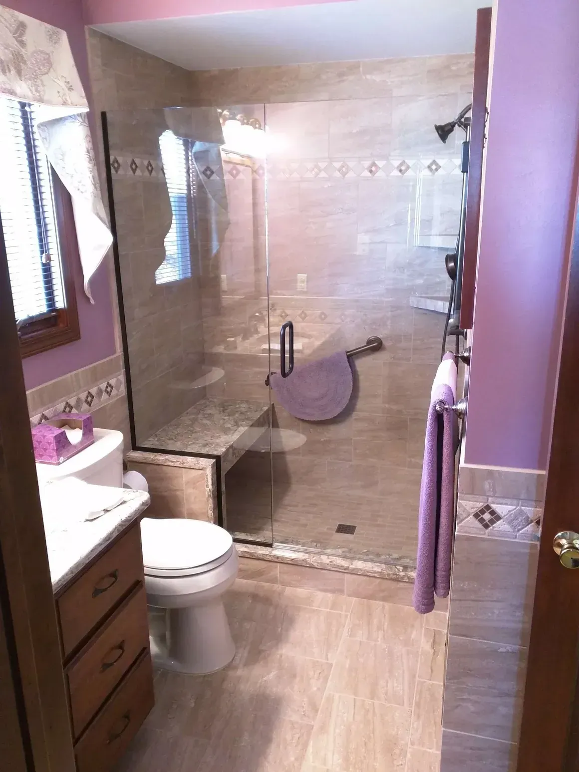 A modern bathroom with light tile floors, a glass-enclosed shower, a toilet, and purple painted walls.