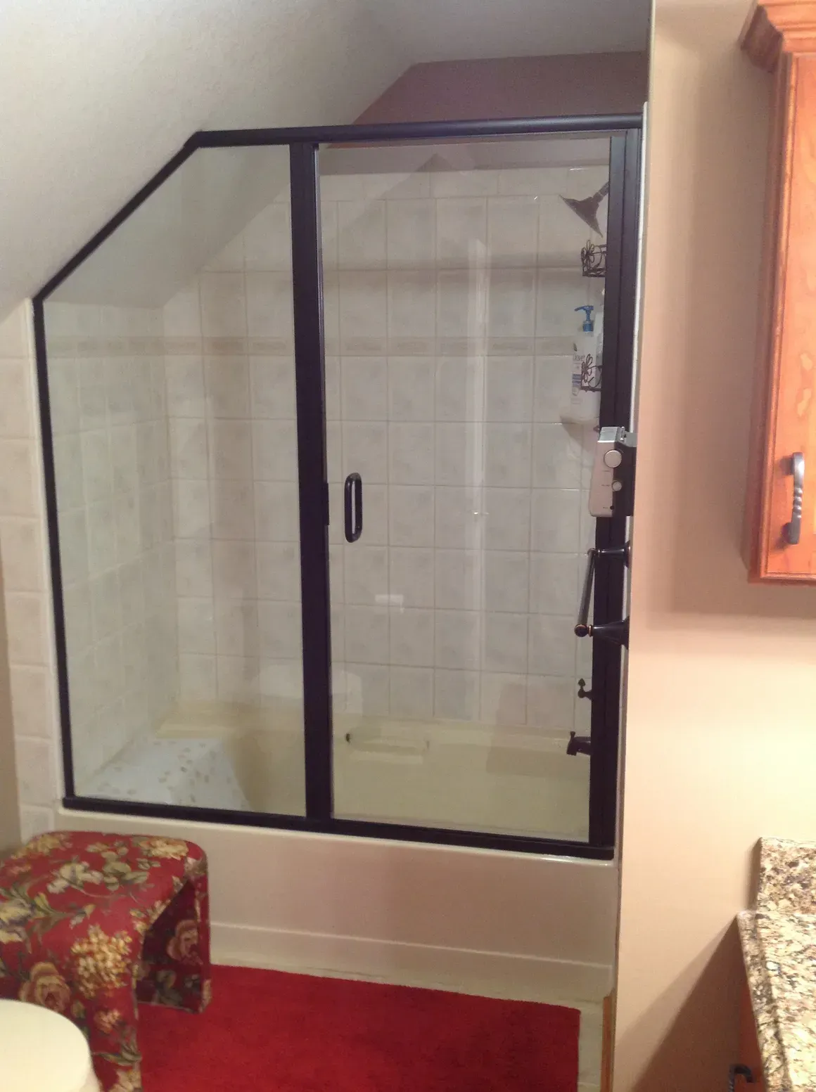 A glass shower enclosure with a black frame installed in a bathroom under a sloped ceiling.