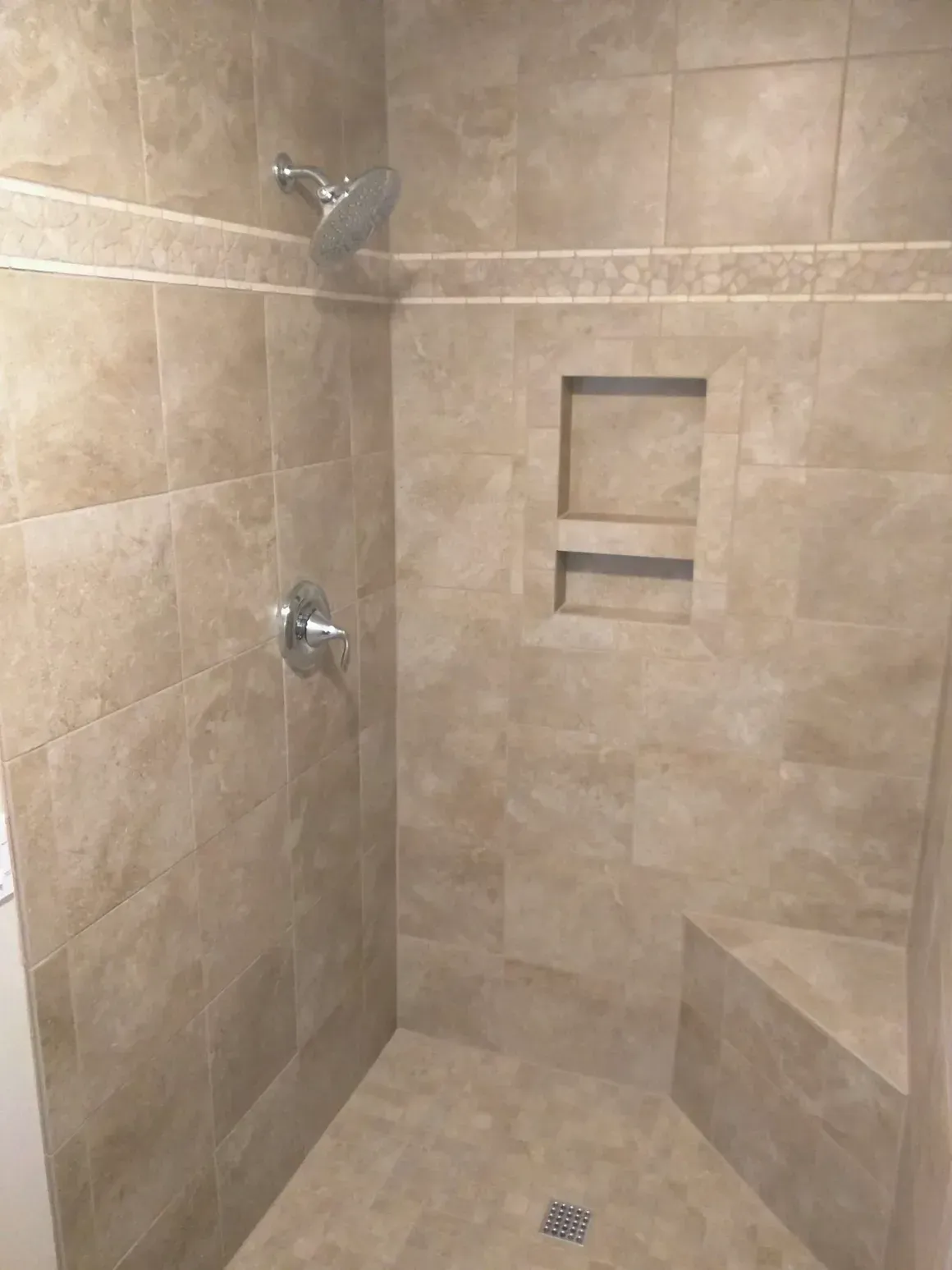 A tiled shower with a corner seat, a built-in recessed shelf, a chrome showerhead, and a single-handle faucet.