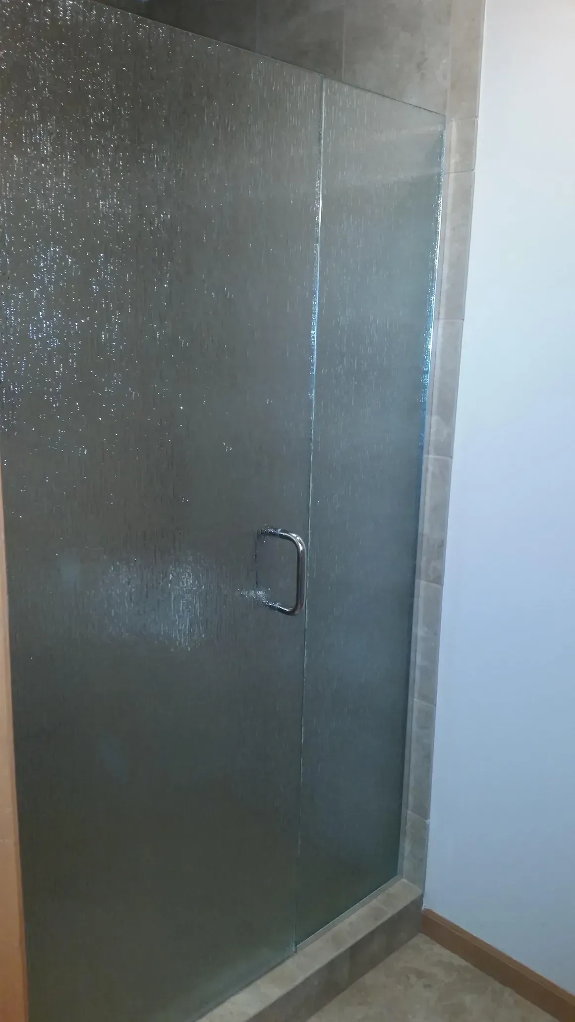 A textured, semi-opaque glass shower door with a polished metal handle set in a tiled bathroom.