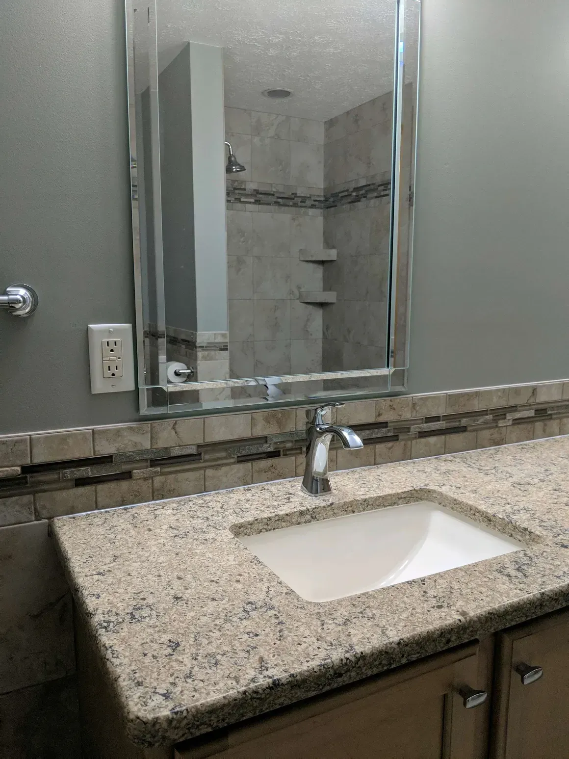 A bathroom vanity with a beige granite countertop, chrome faucet, white sink, and a rectangular mirror above.