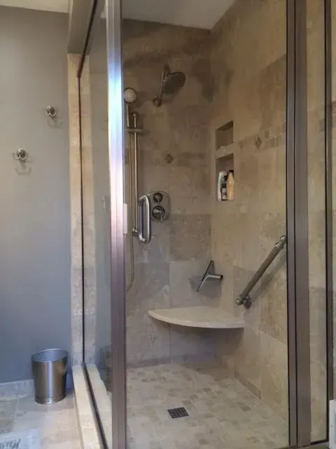 A tiled walk-in shower with a built-in corner seat, grab bars, handheld shower head, and a recessed shampoo niche.