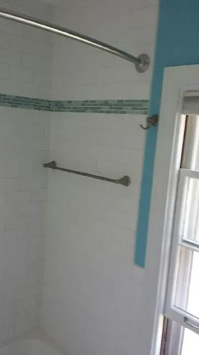A bathroom shower stall with white tiled walls, a horizontal mosaic tile accent strip, and a chrome towel bar and rod.