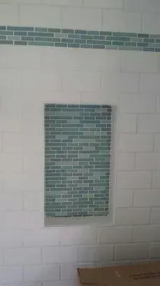 White subway tile shower wall with a horizontal decorative blue glass border and a recessed shower niche.