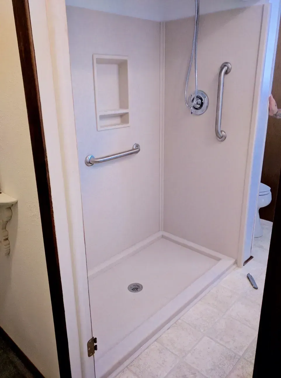 Accessible walk-in shower with beige walls, grab bars, a recessed soap shelf, and a chrome shower control fixture.
