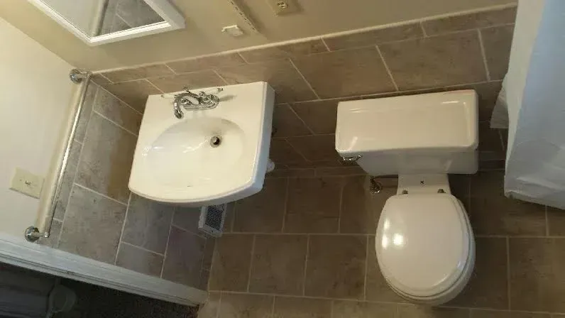 A small bathroom with a wall-mounted white sink next to a white toilet, set against brown tiled walls and floor.