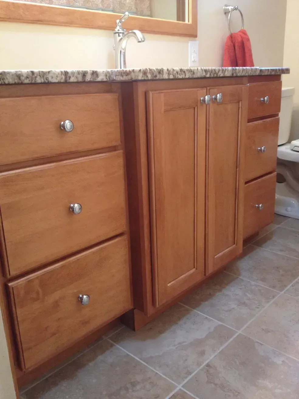A wooden bathroom vanity with granite countertop, silver knobs, and a double-door cabinet flanked by drawers.
