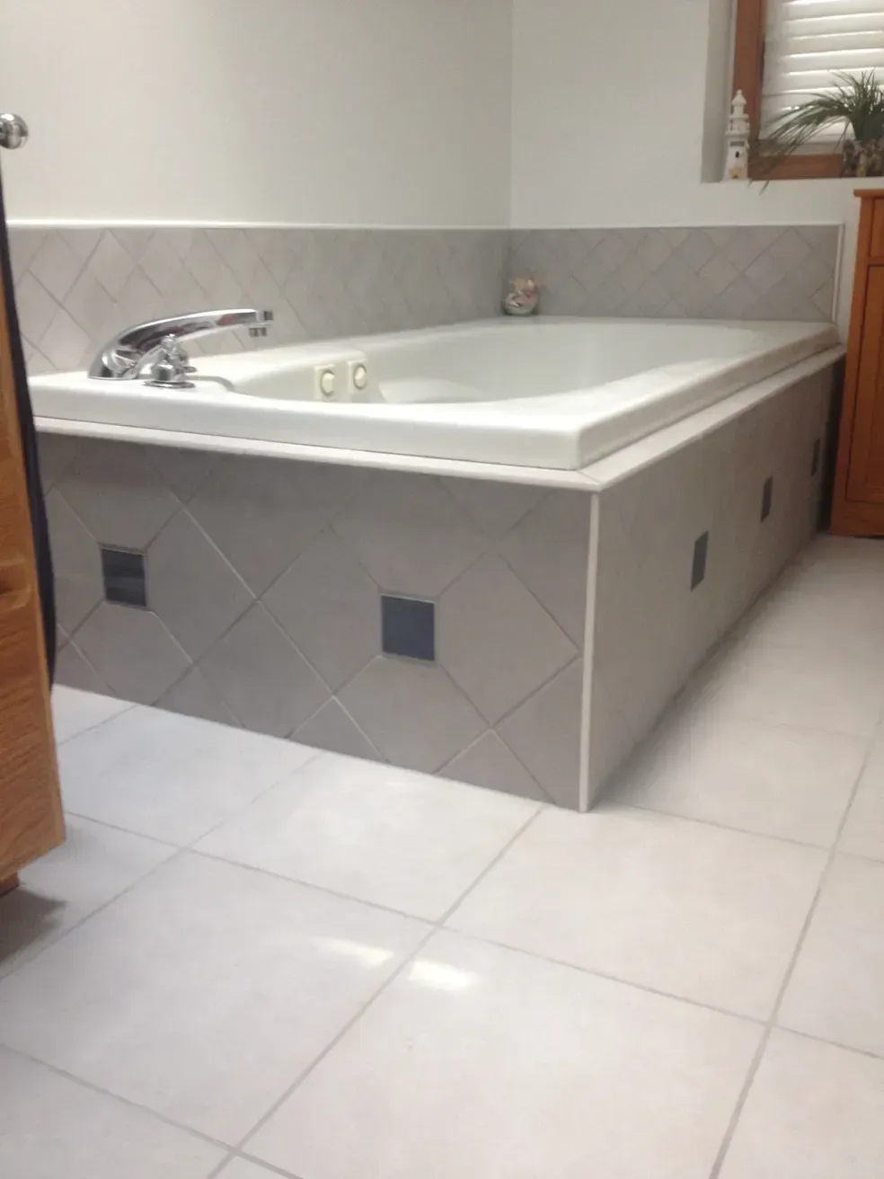 A white bathtub with a chrome faucet set against a wall tiled with light gray diamonds and small, dark accent squares.