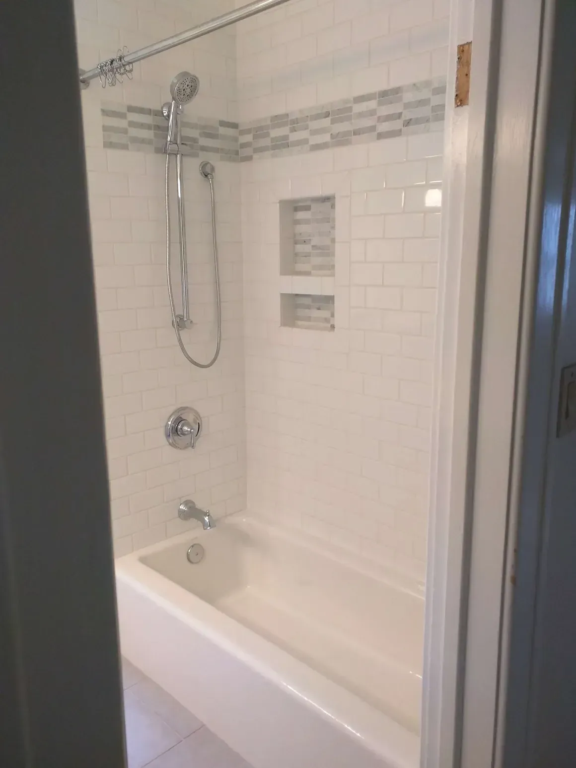A modern white subway tile bathtub shower combination with a handheld shower head and two recessed wall niches.