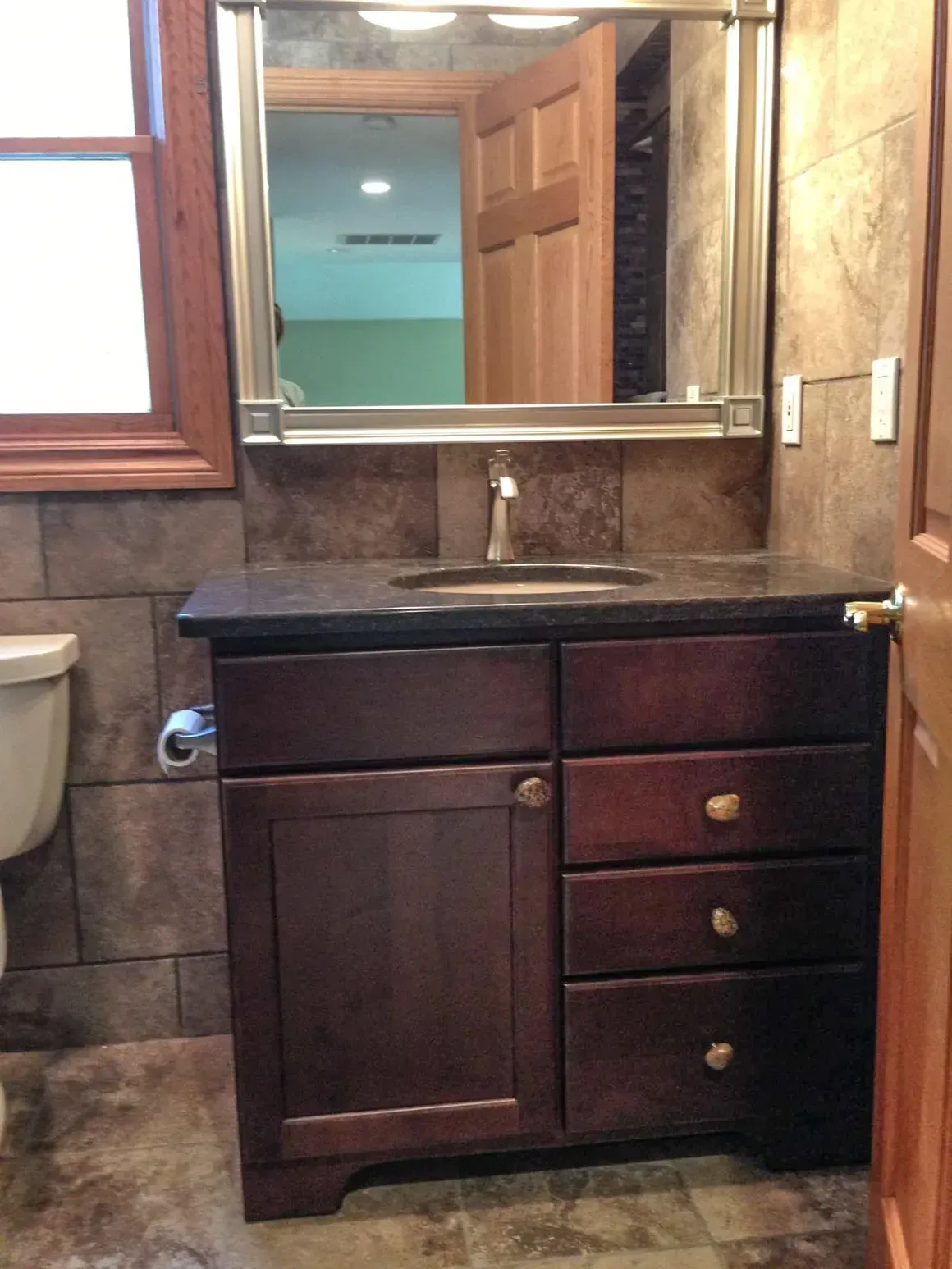 A dark wood bathroom vanity with a black stone countertop, a silver faucet, and a rectangular mirror above.