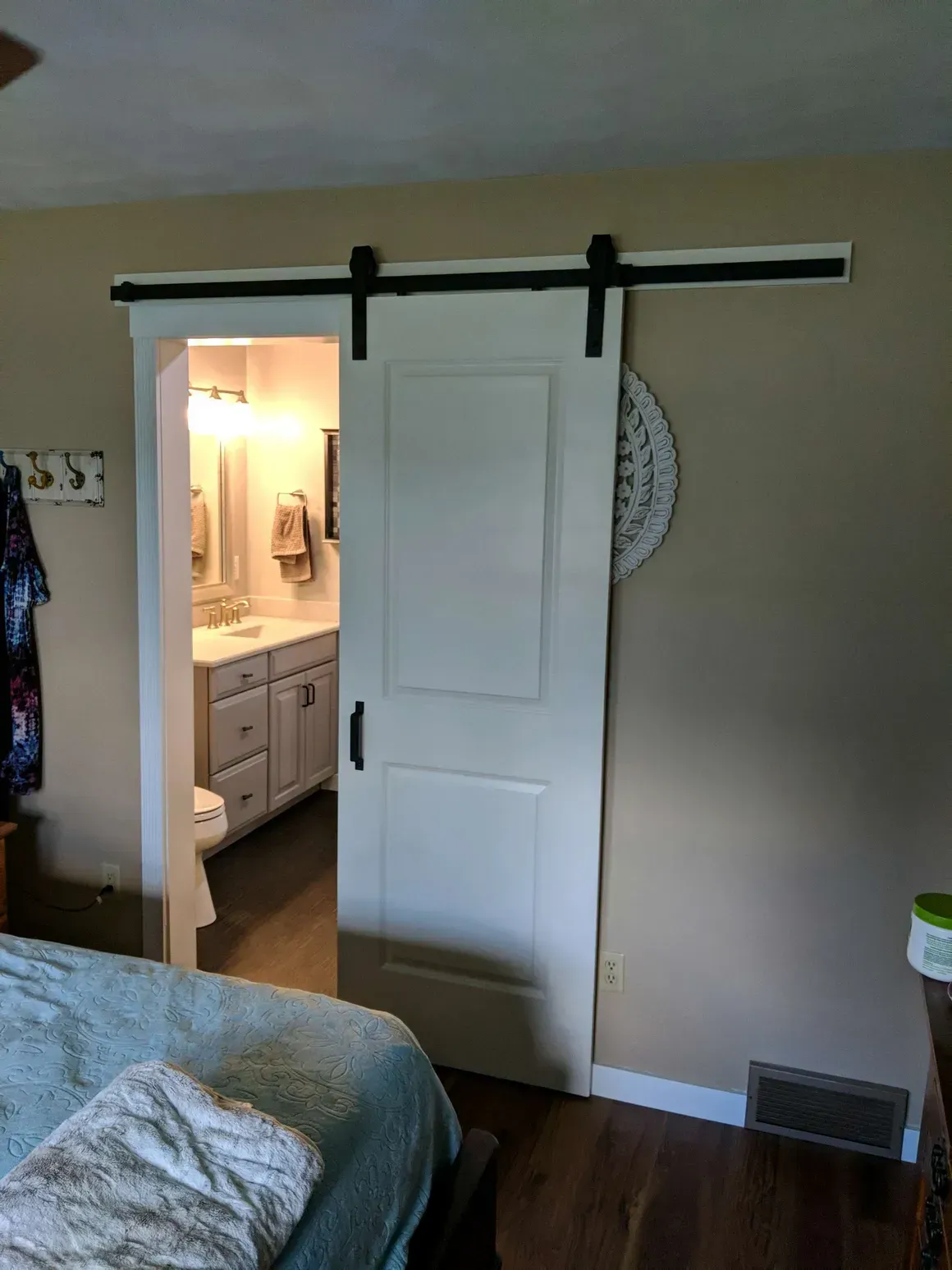 White sliding barn door installed on a black hardware track, partially obscuring the view of a bathroom vanity.