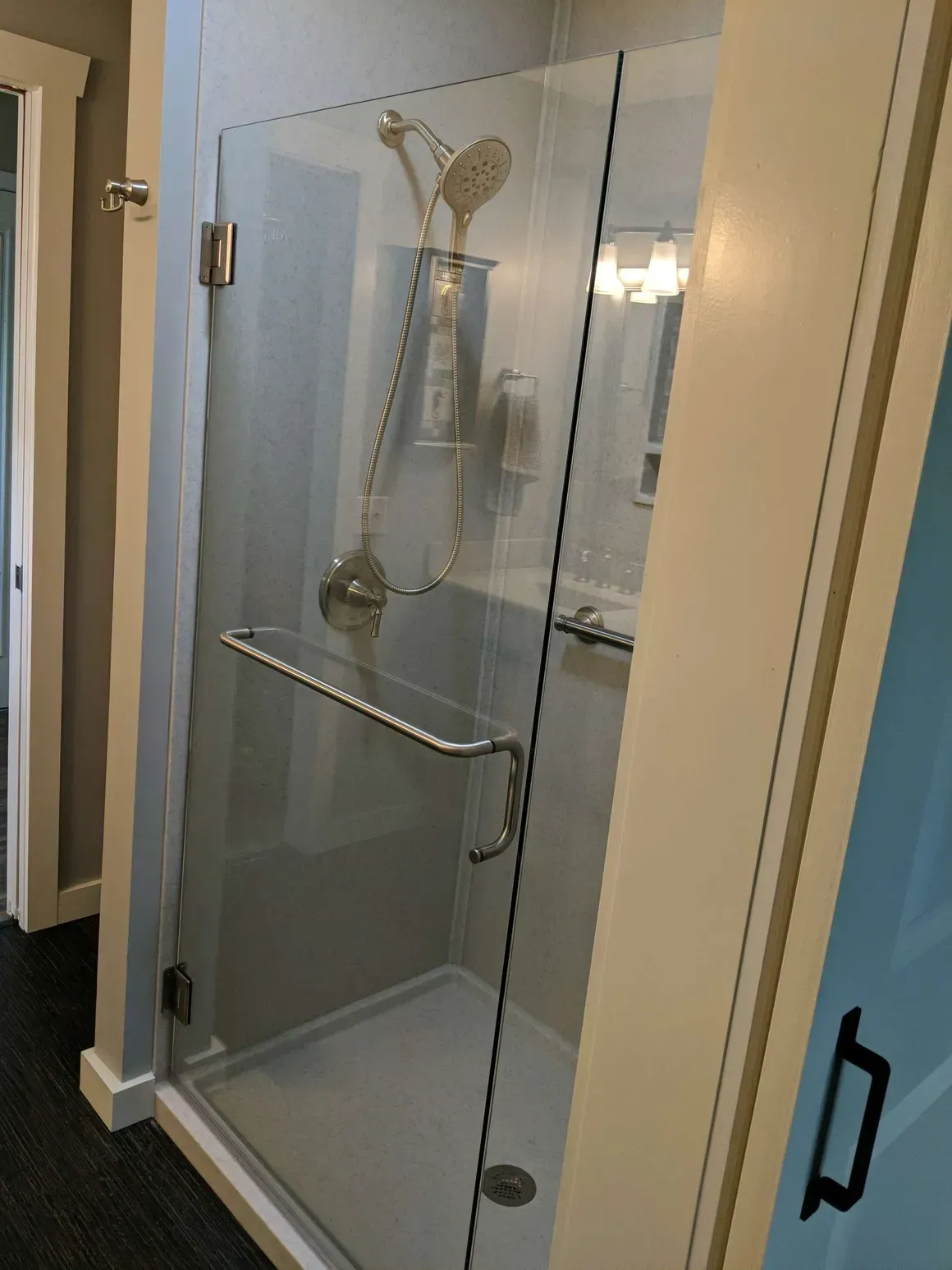 A corner walk-in shower with a glass door, metal handle, and chrome showerhead inside a bathroom.