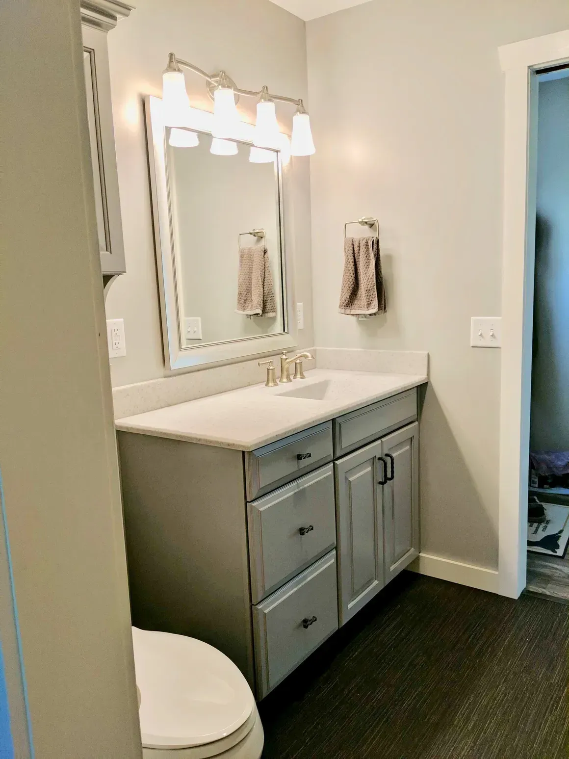 A neutral-toned bathroom featuring a gray vanity with a light countertop, a rectangular mirror, and a wall-mounted light.