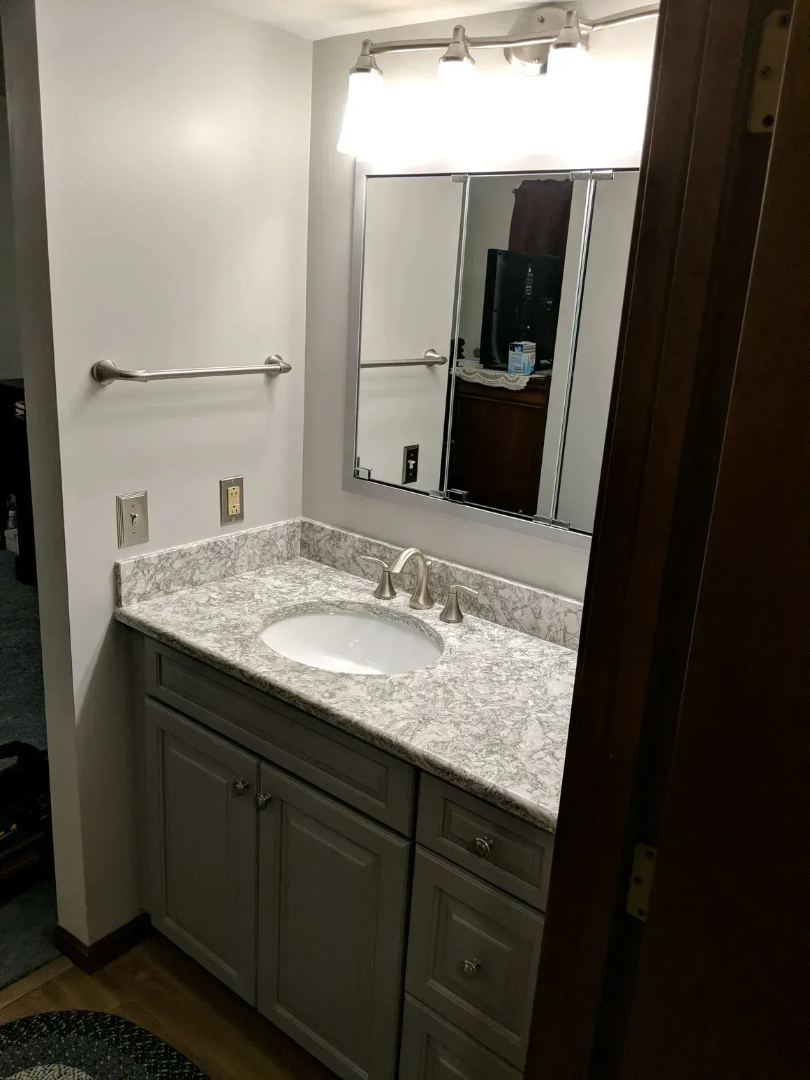 A bathroom vanity with a speckled granite countertop, white sink, gray cabinets, silver faucet, and a large mirror.