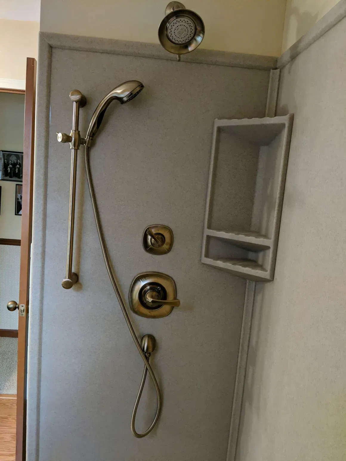 A shower wall with an overhead showerhead, a handheld shower unit on a sliding bar, two controls, and a storage niche.