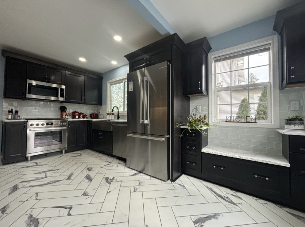 Modern kitchen with dark cabinets, stainless steel appliances, and white marble-look chevron tile flooring.
