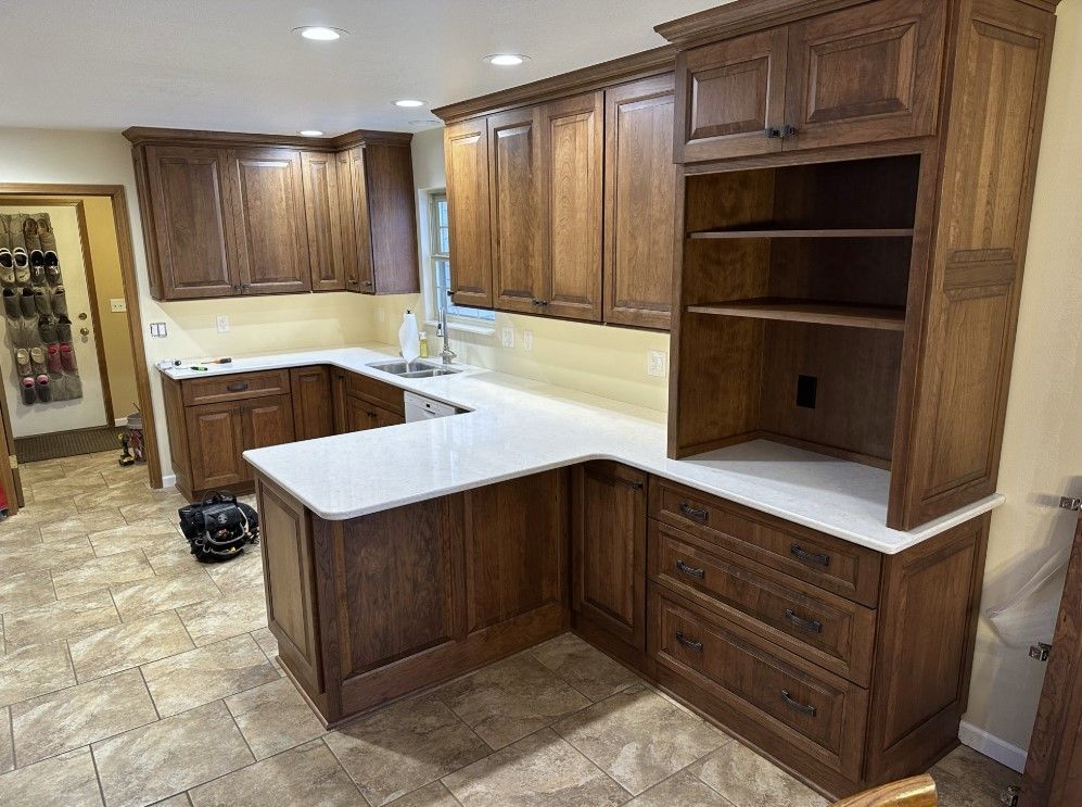 A kitchen featuring dark wood cabinets, white countertops, a corner peninsula, and beige tile flooring.