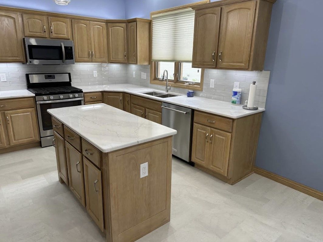 A kitchen with oak cabinets, a white countertop island, stainless steel appliances, and light blue walls.
