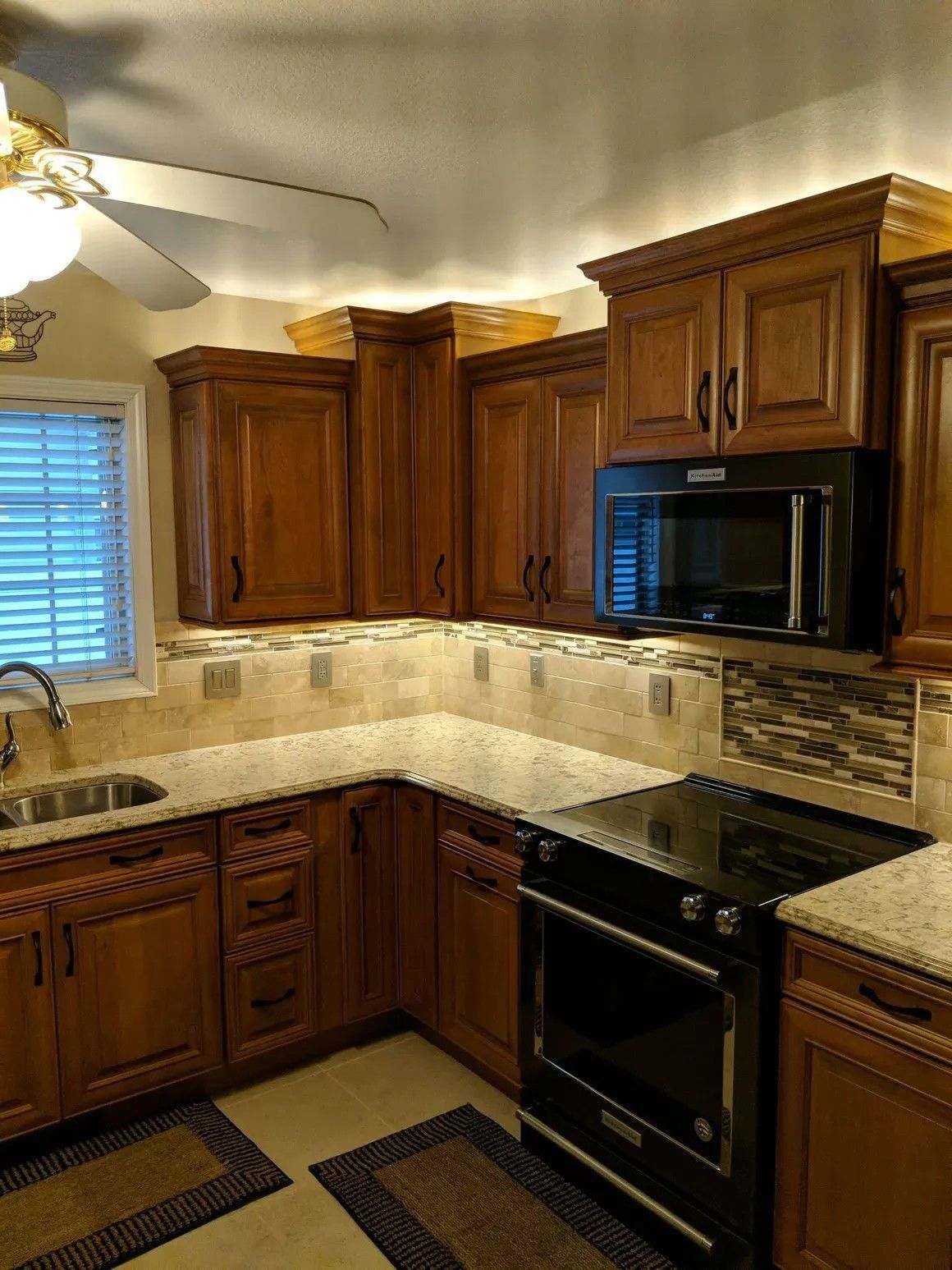 A kitchen with oak cabinets, granite countertops, a tiled backsplash, and a black microwave and range.