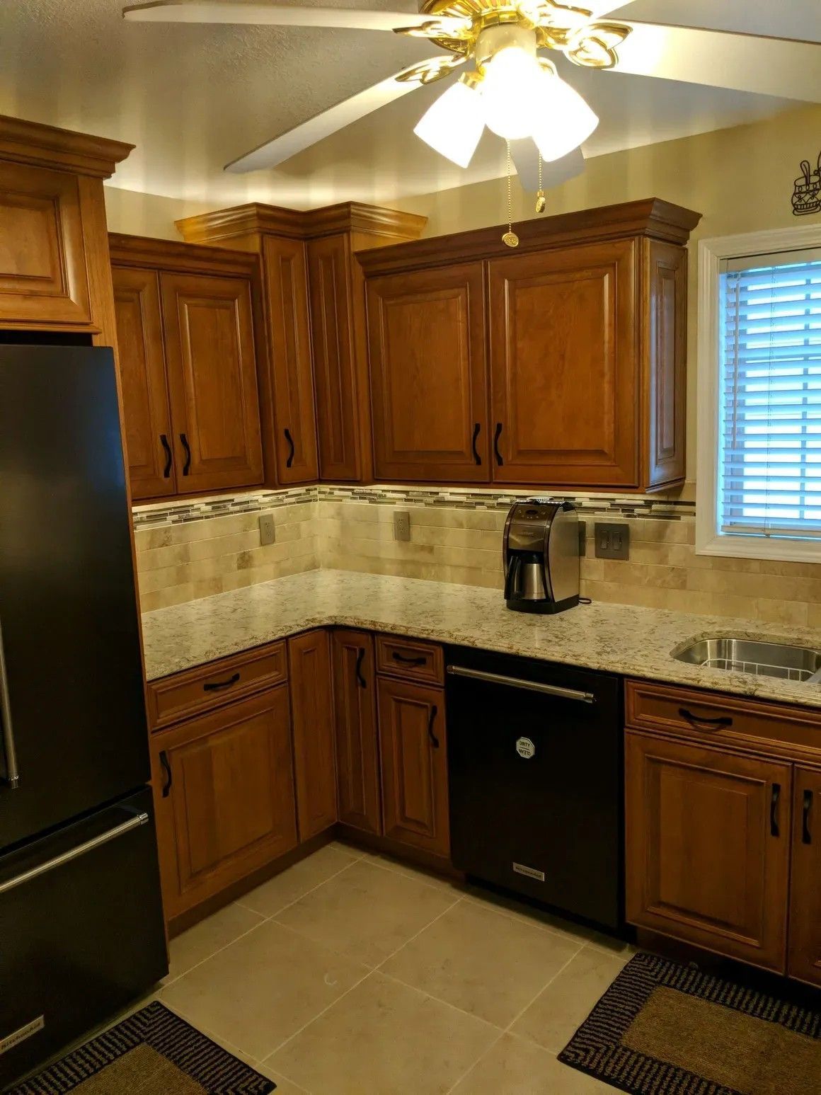 A kitchen with oak cabinets, granite countertops, a stone tile backsplash, and black appliances.