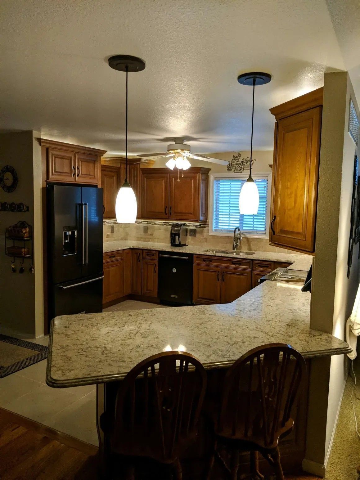 A kitchen features wood cabinets, granite countertops, two pendant lights over a breakfast bar, and black appliances.