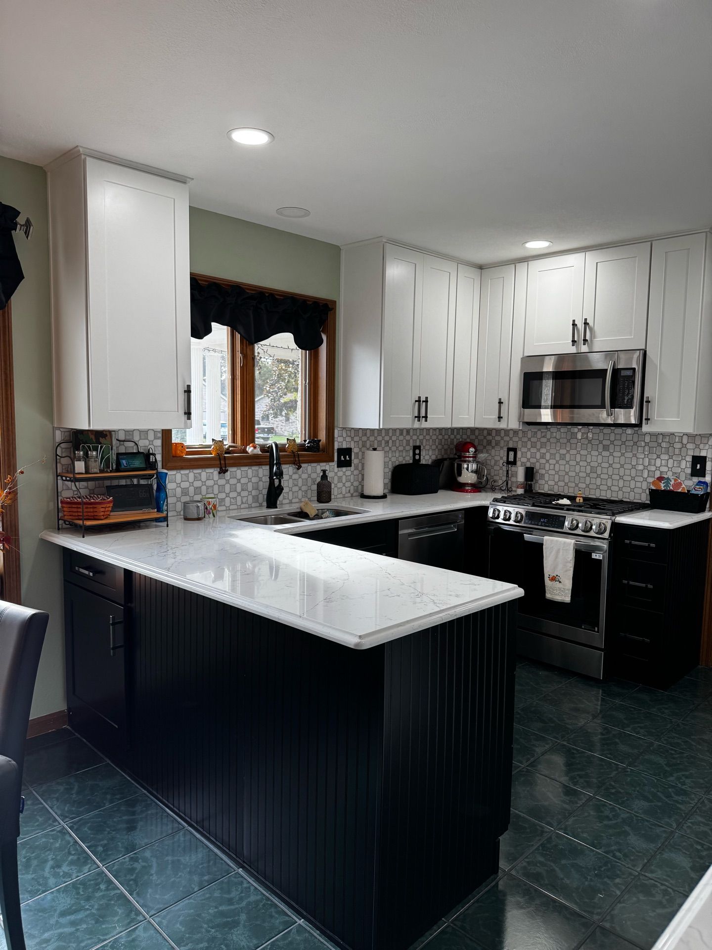 Modern kitchen with white cabinets, dark island, black countertops, and a window above the sink