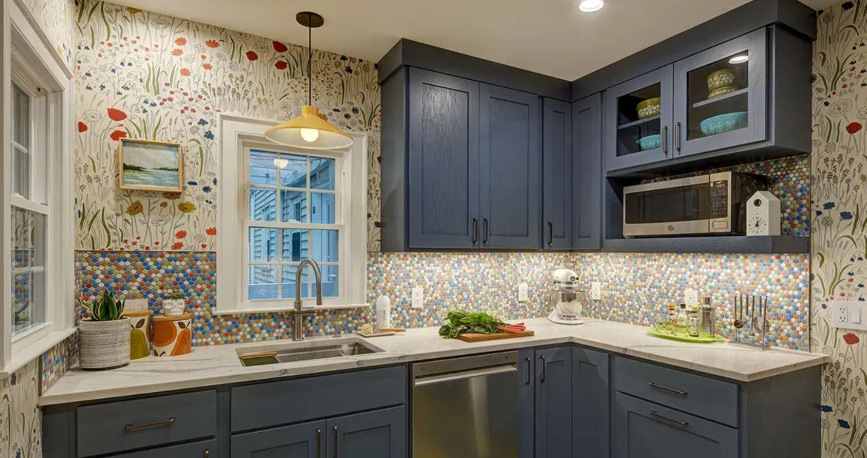 Modern kitchen with dark blue cabinets, patterned wallpaper, stainless appliances, and a window over the sink.