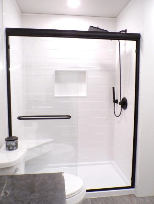 Bathroom shower with black-framed glass door, white tile walls, and a built-in shelf niche.