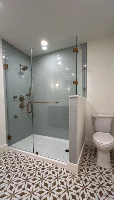 Modern bathroom with glass shower enclosure, white tile walls, and a toilet beside patterned floor tiles