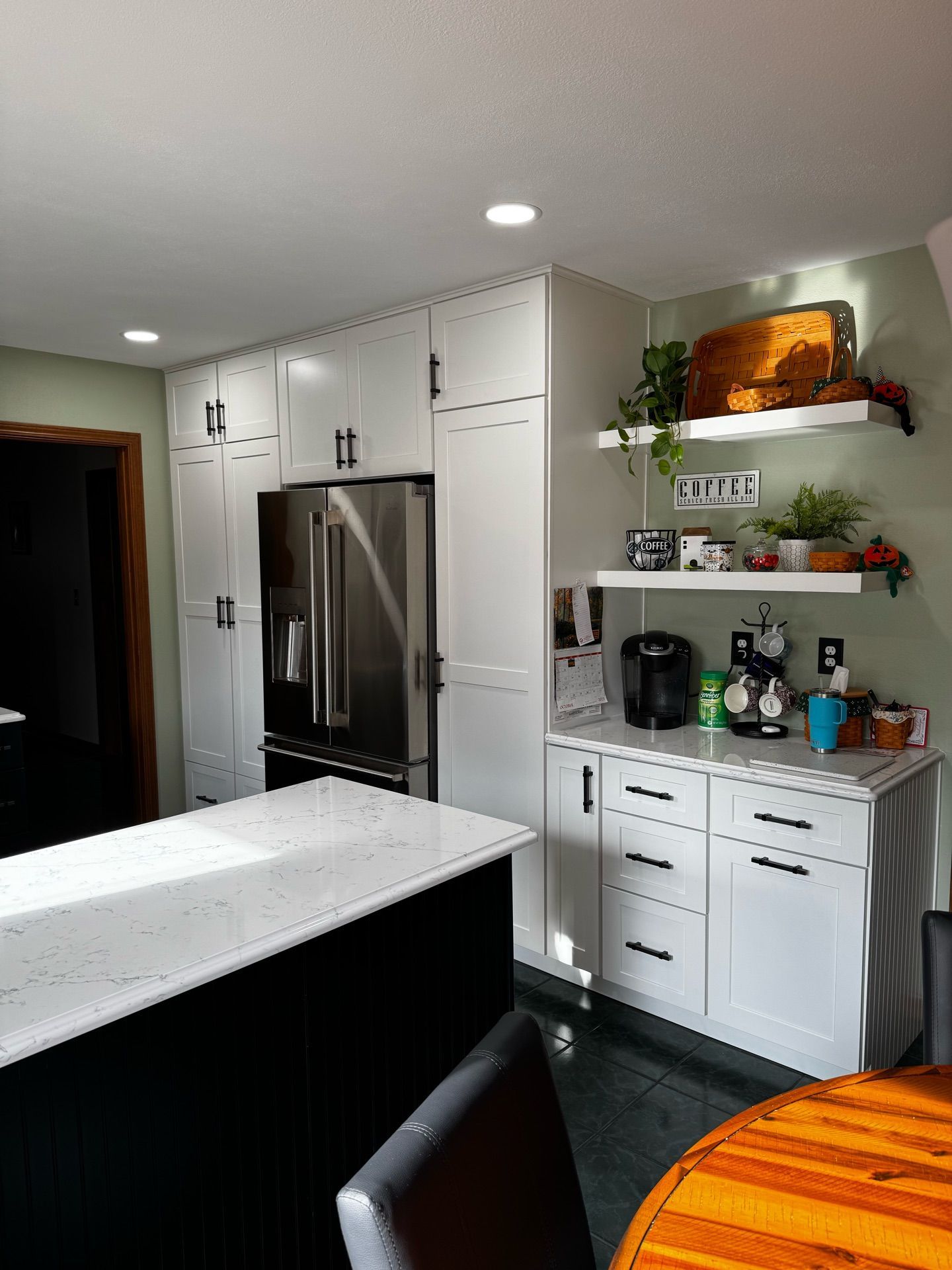 Modern kitchen with white cabinets, stainless steel fridge, island, and open shelves with plants and decor